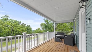A covered porch with a wooden deck, white railing, and outdoor furniture.