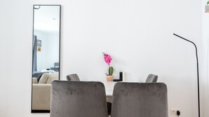 A modern dining area with two grey upholstered chairs, a wooden floor, a white wall, a mirror, a small potted plant, and a floor lamp.