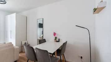 Une pièce moderne et minimaliste, avec une table à manger blanche, des chaises grises, une petite plante en pot et un miroir au mur.
