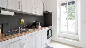 A modern kitchen with light wood cabinets, a stainless steel sink, a coffee maker, and a window with a view of greenery.