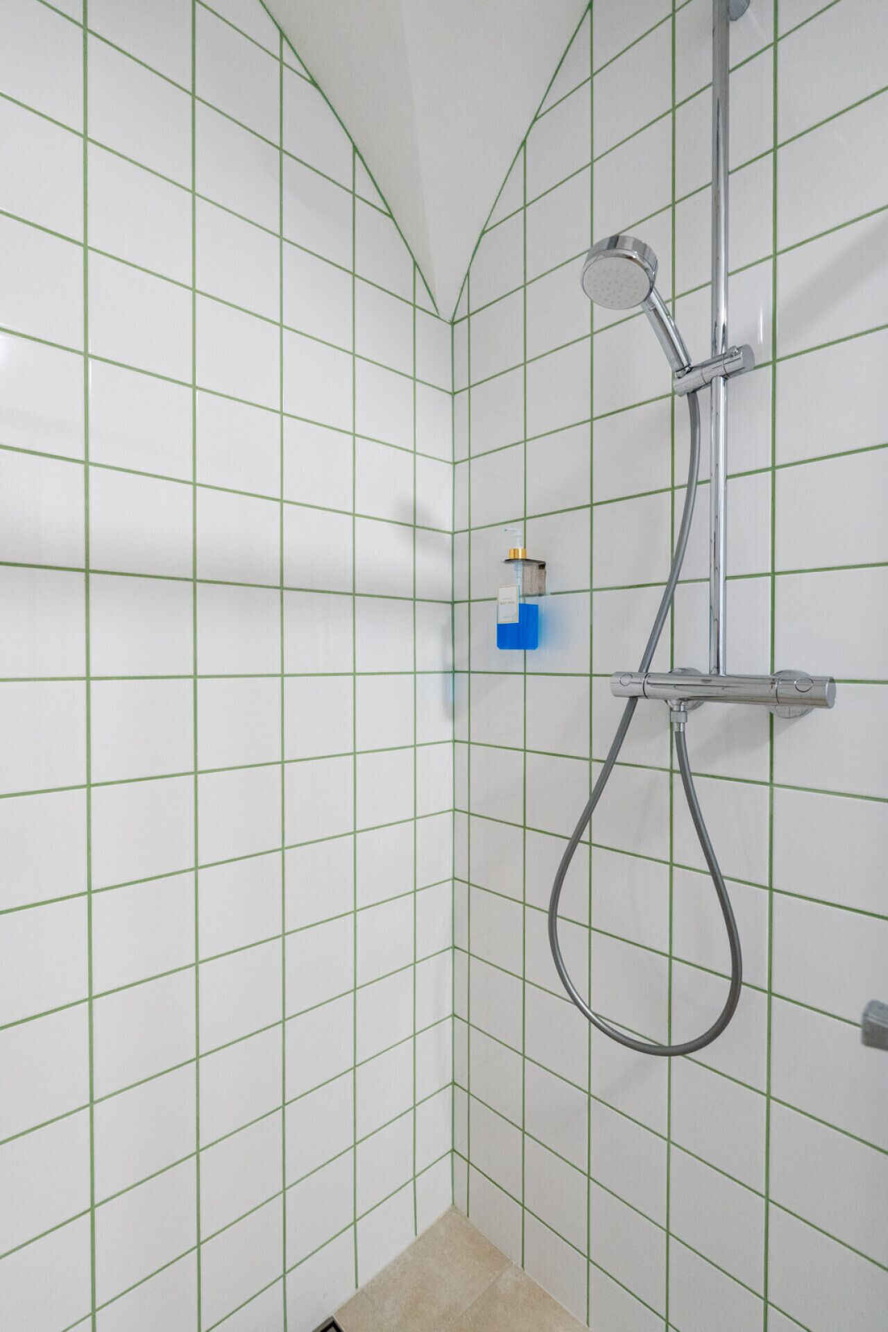 A shower with a handheld showerhead and a wall-mounted faucet in a tiled bathroom.