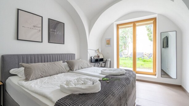 A bedroom with a bed, a desk, and a large window.