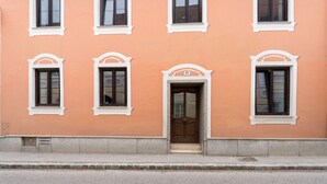 A building with a peach-colored facade, white window frames, and a central door with a number plaque.