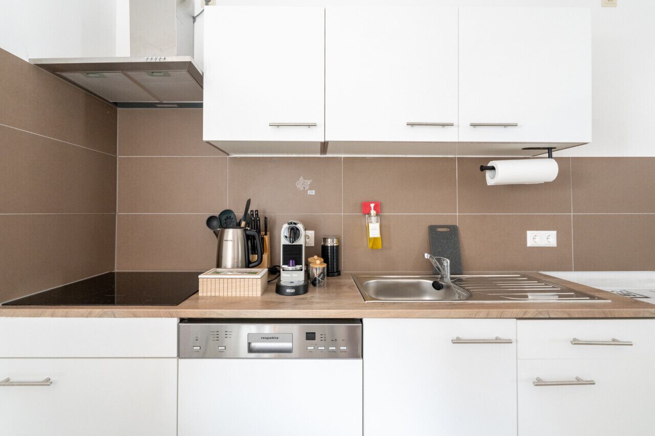 Une cuisine moderne avec des meubles blancs, un lave-vaisselle intégré et une machine à café.