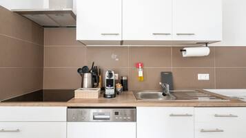 Une cuisine moderne avec des meubles blancs, un lave-vaisselle intégré et une machine à café.
