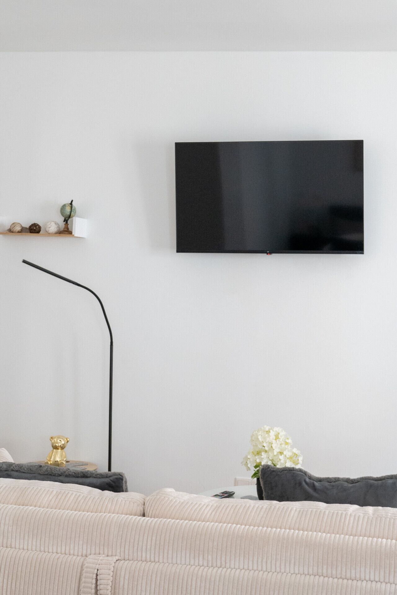 Una sala de estar moderna con un televisor de pantalla plana en la pared, una lámpara de pie, un sofá y una pequeña mesa con adornos.