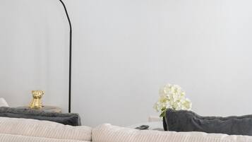 Una sala de estar moderna con un televisor de pantalla plana en la pared, una lámpara de pie, un sofá y una pequeña mesa con adornos.