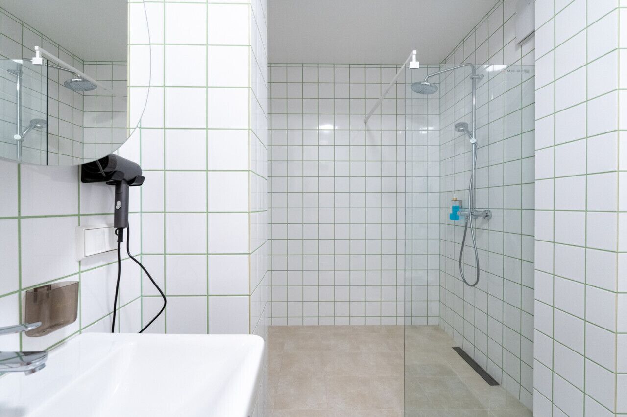 Een moderne badkamer met witte betegelde wanden, een glazen douchecabine en een witte wastafel.