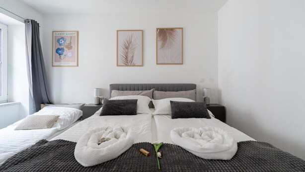 Ein modernes Hotelzimmer mit einem großen Bett, zwei Nachttischen, einem Fenster mit Vorhängen und gerahmten Kunstwerken an der Wand.