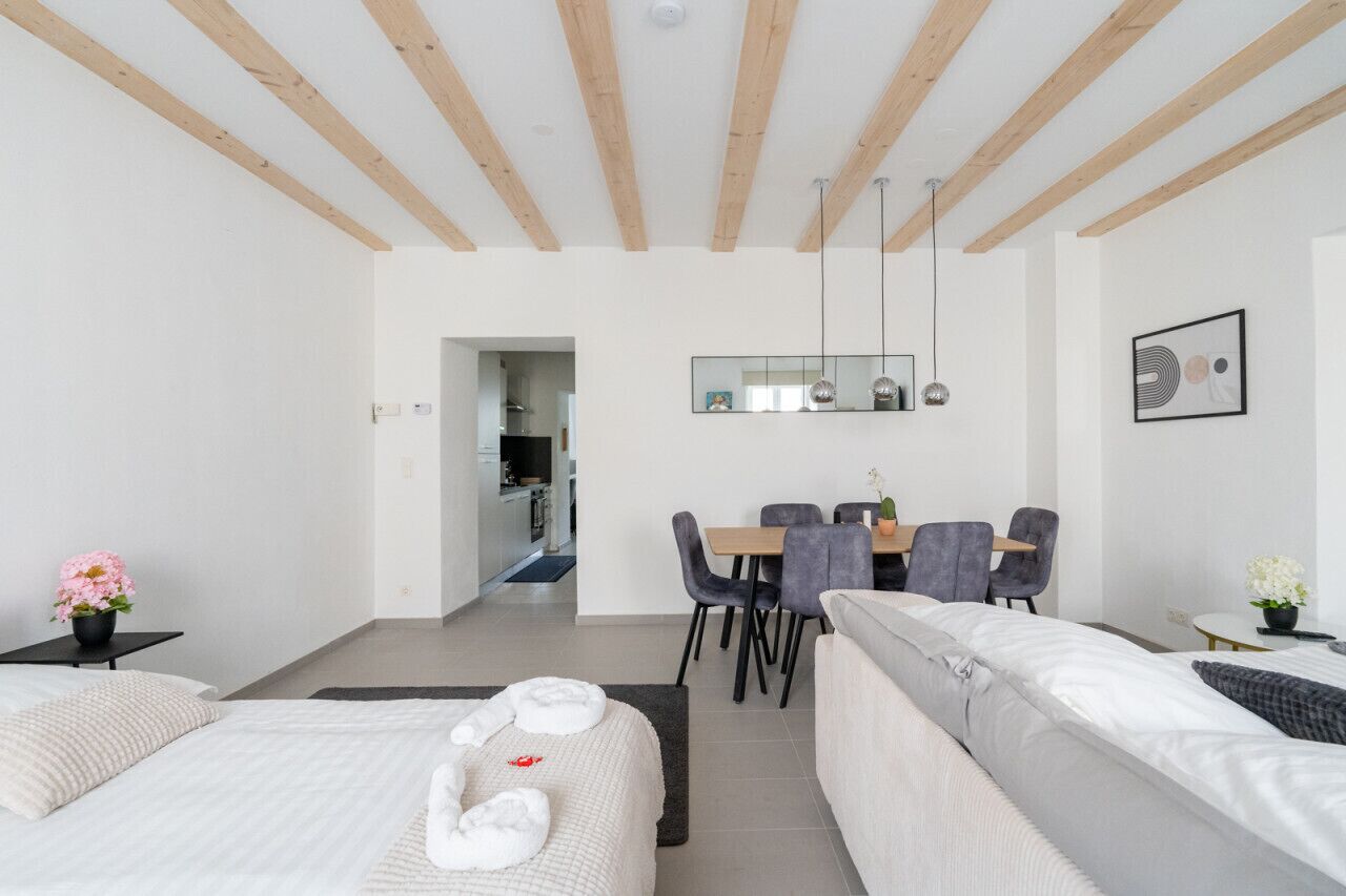 A modern hotel room with a wooden ceiling, a dining area with a table and chairs, and a separate living area with a sofa.