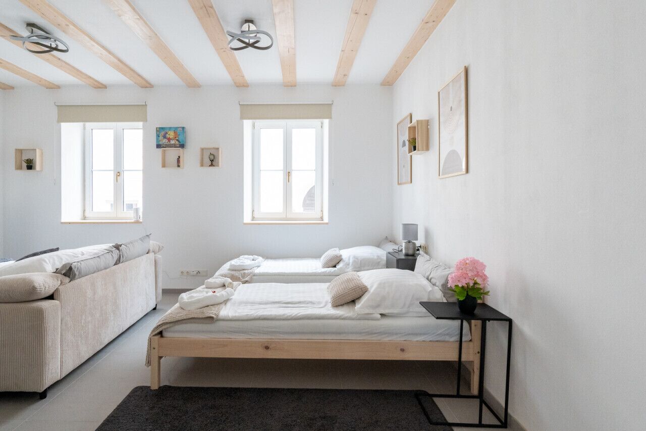 A minimalist bedroom with two beds, a sofa, and a small table with a flower.