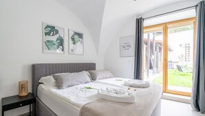 Una camera da letto moderna con un letto grande, un comodino e vista su un giardino tramite una porta scorrevole.