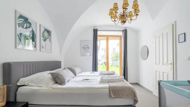 Camera da letto con un letto grande, un lampadario, vista sull'esterno e una porta con uno specchio.