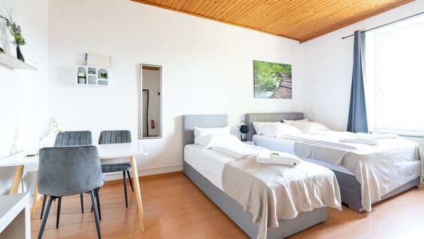 A modern bedroom with two beds, a desk, and a chair.