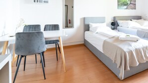 A hotel room with two beds, a dining table with chairs, and a small desk.