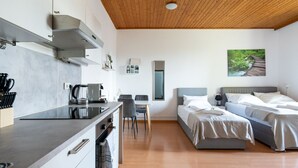 A modern hotel room with a kitchenette, two beds, a dining area, and a large window.