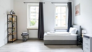 Une chambre moderne avec un lit, un radiateur, une fenêtre avec des rideaux, une étagère sur laquelle est posé un vélo, et un cache-radiateur.
