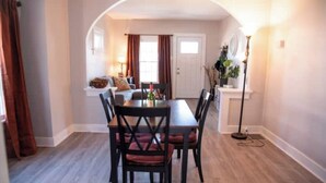 A dining area with a table and chairs, a lamp, and a view into a living room with a sofa and curtains. - Blueberry Bungalow with Stunning Patio & Garden (Dayton)