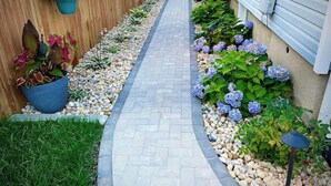 A narrow pathway flanked by a wooden fence and a house with a blue exterior. - Blueberry Bungalow with Stunning Patio & Garden (Dayton)