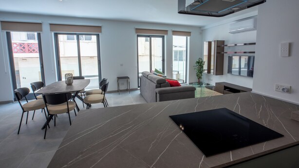 A modern kitchen with a large island, dining area with chairs, and a sofa.