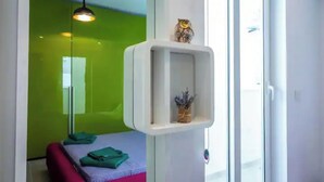 A room with a green wall, a white shelf with an owl decoration, a hanging light, and a bed with green and pink bedding.