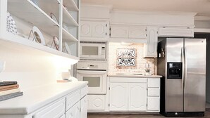A modern kitchen with white cabinetry, a stainless steel refrigerator, and a microwave above the oven. - The Cozy Home near Lancium, ACU, HSU, Hendrick (Abilene)