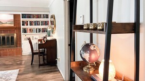A cozy living room with a fireplace, a bookshelf, a globe, and a desk with a lamp. - The Cozy Home near Lancium, ACU, HSU, Hendrick (Abilene)