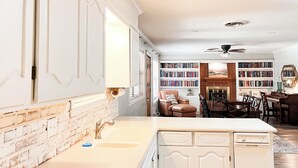 A kitchen with white cabinetry, a brick accent wall, a dining area with a piano, and a fireplace. - The Cozy Home near Lancium, ACU, HSU, Hendrick (Abilene)