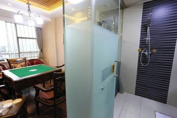 Une table de billard dans une pièce séparée par une cloison en verre, un espace douche avec un mur recouvert de carreaux noirs, et un coin repas avec des chaises et une table.