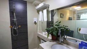 A modern bathroom with a large mirror, a sink, a shower with a handheld showerhead, and a potted plant on the counter.