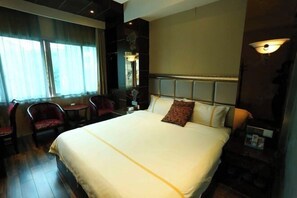 Une chambre d’hôtel avec un grand lit, un bureau, deux chaises, une fenêtre avec des rideaux et une lampe fixée au mur.