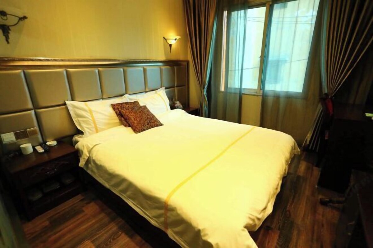 Une chambre d’hôtel avec un lit, une table de chevet, une lampe fixée au mur et une fenêtre avec des rideaux.