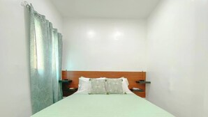 Ein schmales Hotelzimmer mit einem Einzelbett, einem hölzernen Kopfteil und einem Nachttisch mit einer Lampe.