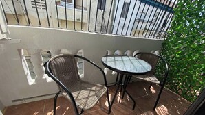 Ein Balkon mit zwei Korbstühlen und einem kleinen runden Tisch, umgeben von einem weißen Geländer und einem gefliesten Boden.