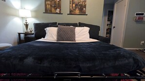 A bed with a dark cover, a bedside table with a lamp, and two paintings on the wall. - Warm & Cozy Home Near SeaWorld/Fiesta TX/Lackland AFB (San Antonio)