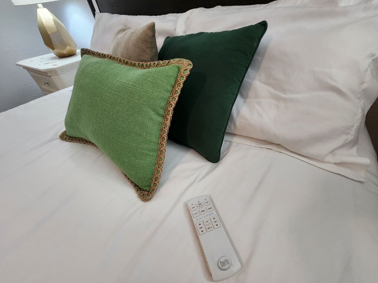 A bed with two pillows, one green and one dark green, and a remote control on the bed.