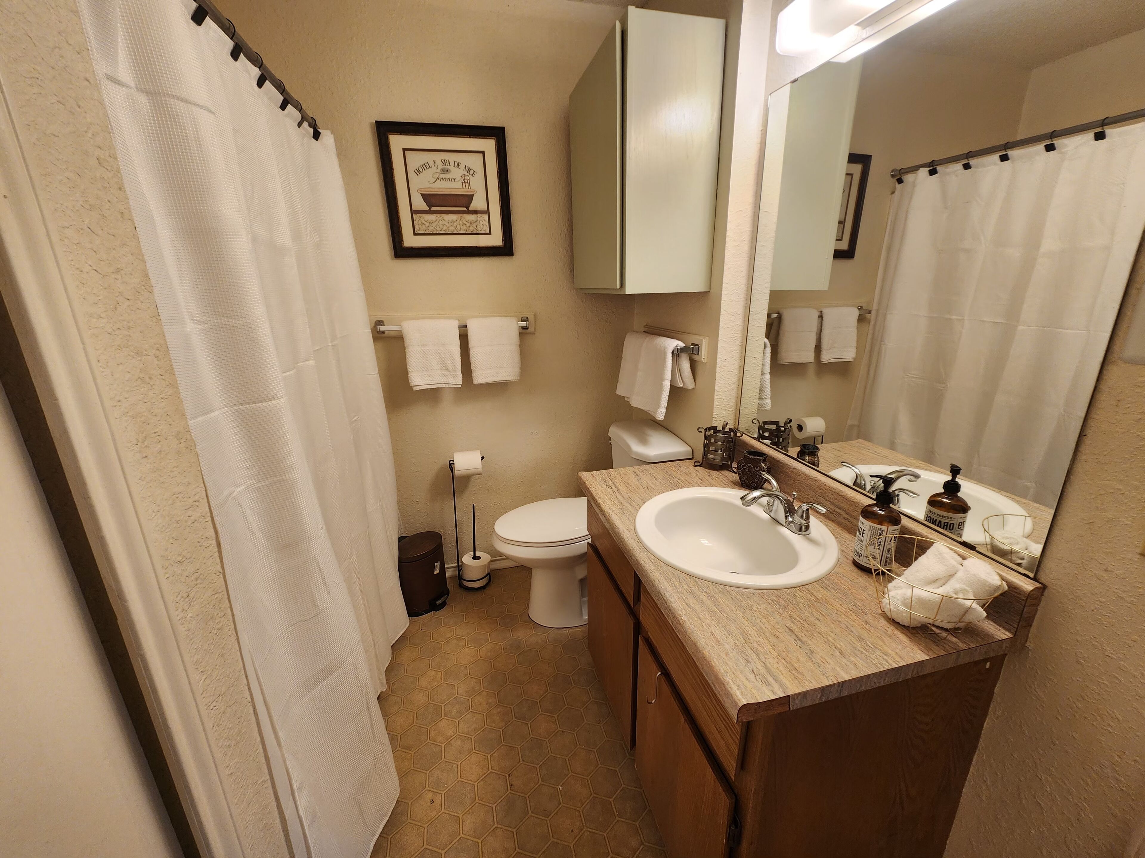 A bathroom with a sink, toilet, and shower curtain. There are towels hanging on the wall and a framed picture above the toilet.