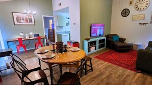 A dining area with a wooden table and chairs, a red rug, a television, and a clock on the wall. - Warm & Cozy Home Near SeaWorld/Fiesta TX/Lackland AFB (San Antonio)