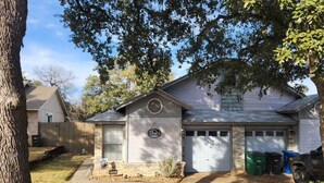 A single-story house with a garage, a front yard with a tree, and a driveway. - Warm & Cozy Home Near SeaWorld/Fiesta TX/Lackland AFB (San Antonio)