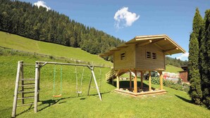 Ein hölzernes Spielhaus mit Schaukeln auf einer grünen Wiese.