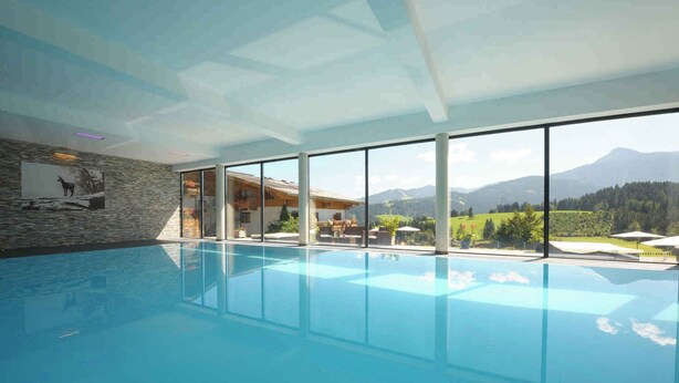 Ein moderner, überdachter Pool mit großen Fenstern und Blick auf die Berge.