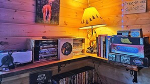 Un coin accueillant avec un mur en bois, une lampe, une collection de livres et un panneau indiquant que des jeux sont mis à disposition gratuitement.