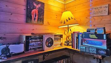 A cozy corner with a wooden wall, a lamp, a collection of books, and a sign indicating free games.