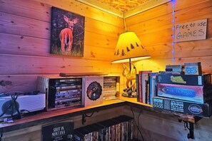 A cozy corner with a wooden wall, a lamp, a collection of books, and a sign indicating free games.