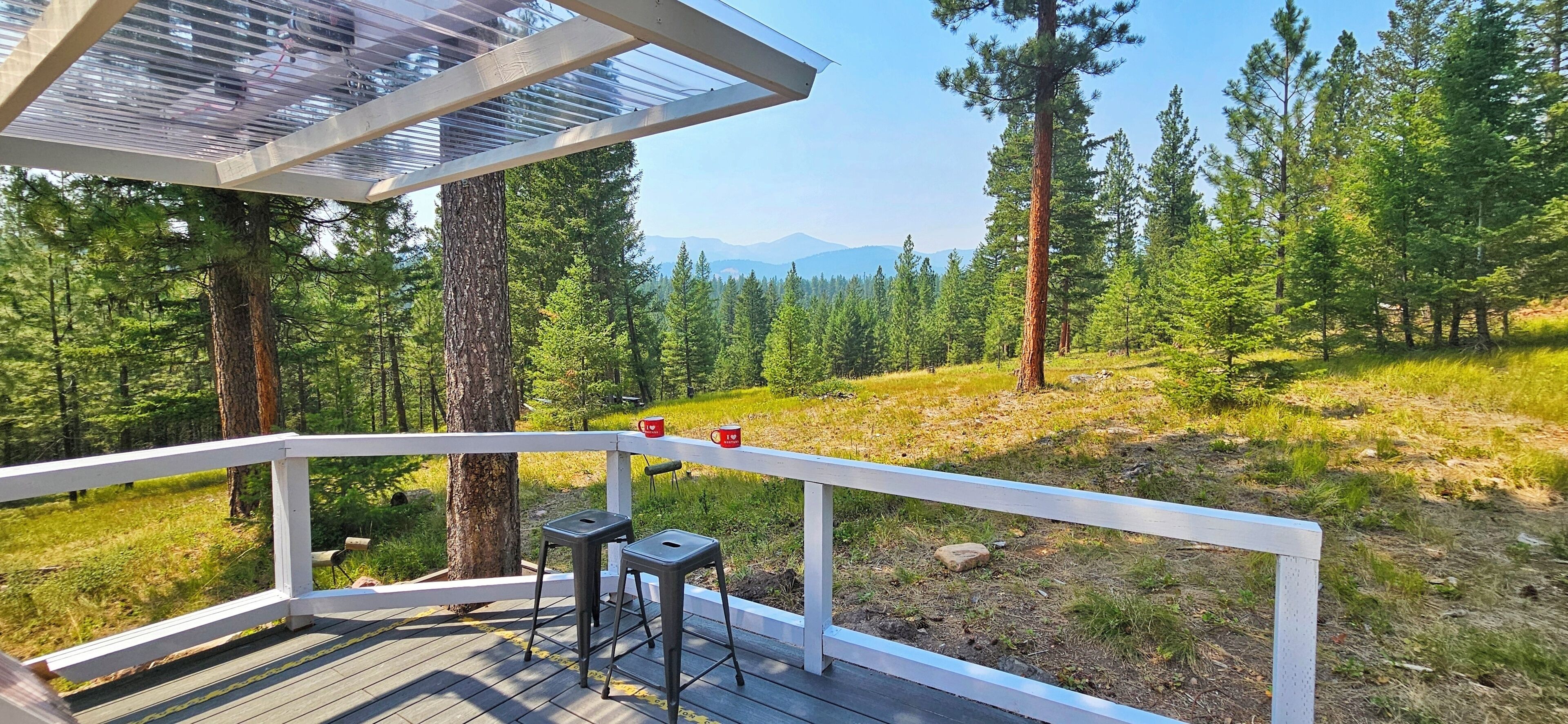A deck with a white railing overlooking a forested area with mountains in the distance.
