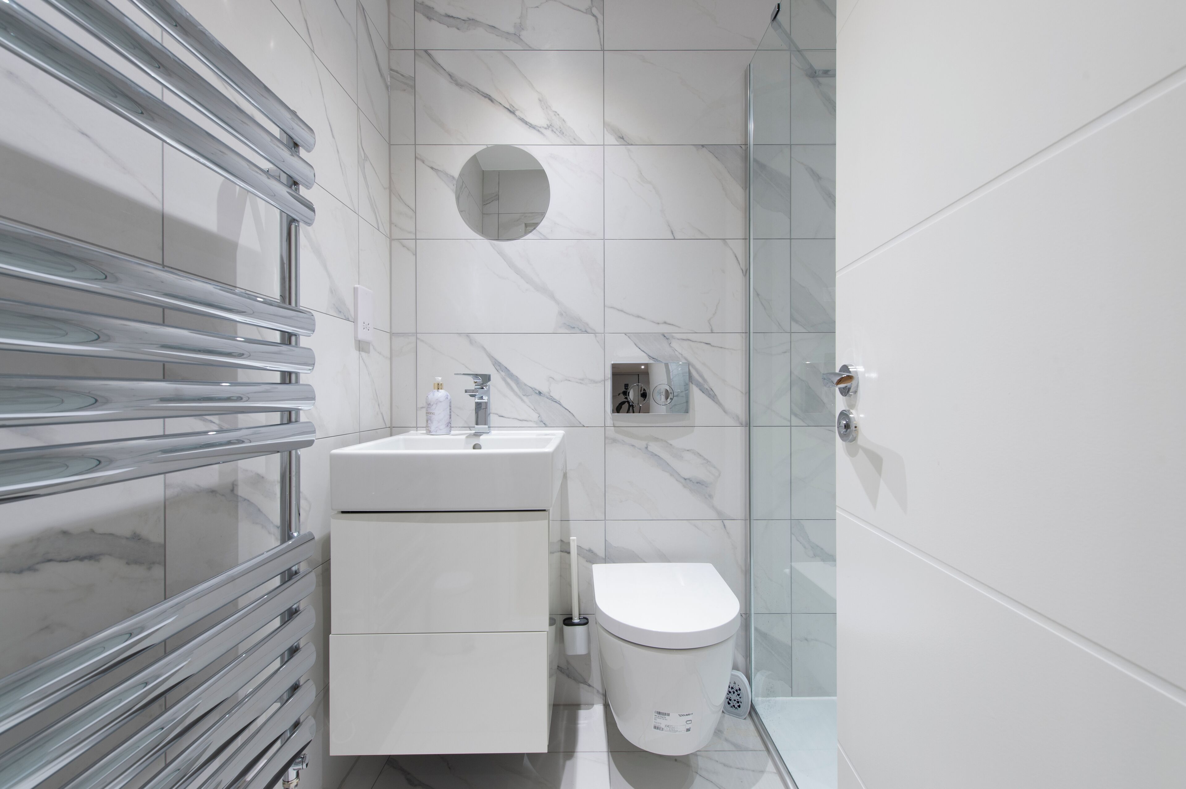 A modern bathroom with a glass shower enclosure, a white sink with a marble countertop, and a toilet.