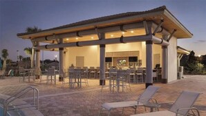An outdoor pool area with lounge chairs, a covered seating area, and a bar. - House near Disney world and many other attractions and theme parks. (Davenport)