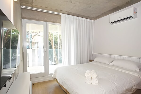 Una habitación de hotel con una cama, un ventanal con cortinas y un equipo de aire acondicionado.
