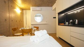 A hotel room with a bed, a round mirror, a small dining table with chairs, and a kitchenette.