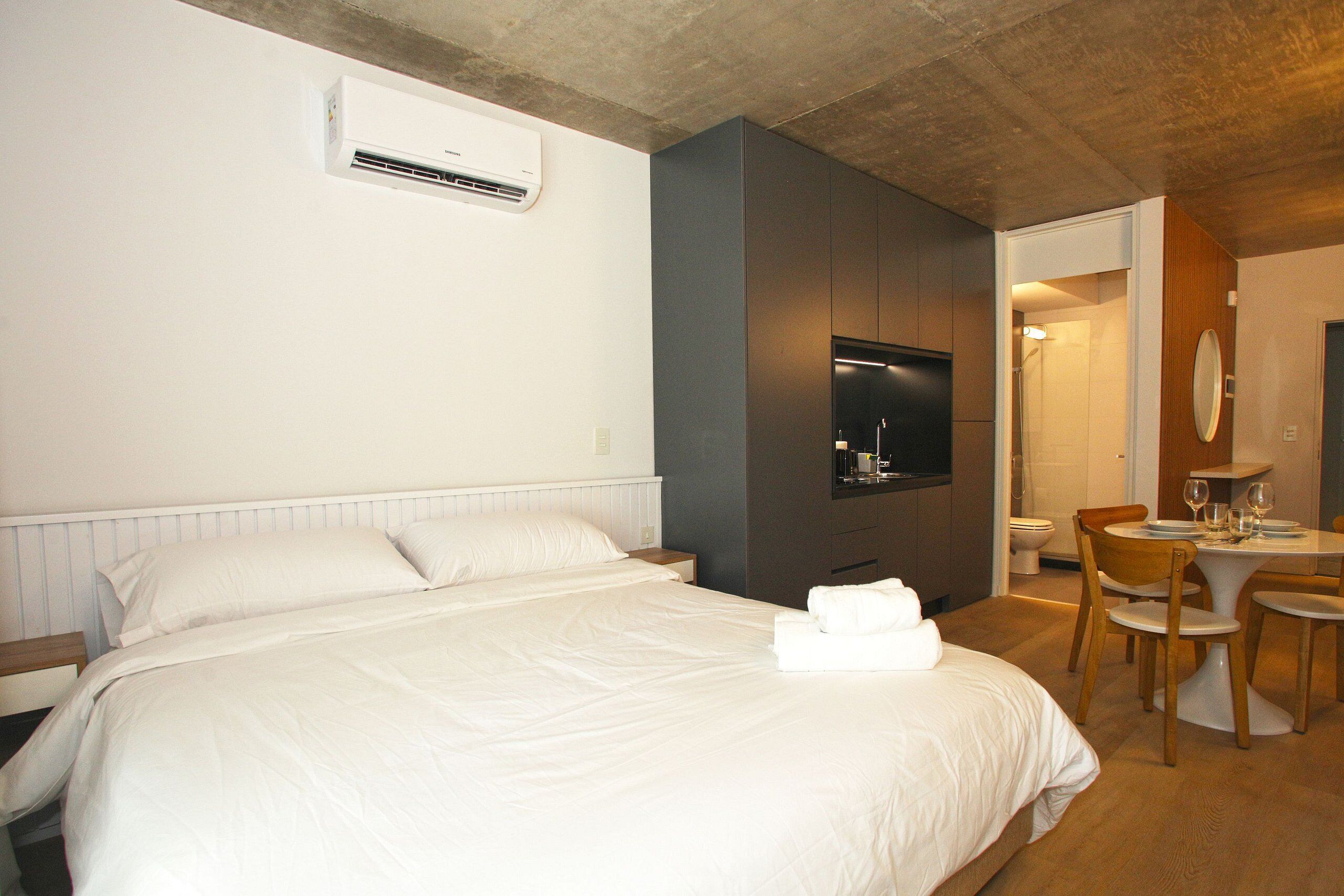 Hotelkamer met een bed, een televisie, een kleine eettafel met stoelen en een badkamer zichtbaar door een open deur.